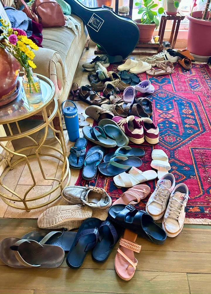 A living room area with multiple pairs of shoes scattered on a patterned red rug at Joytown, a transformational retreat & tantra sanctuary in Colorado.