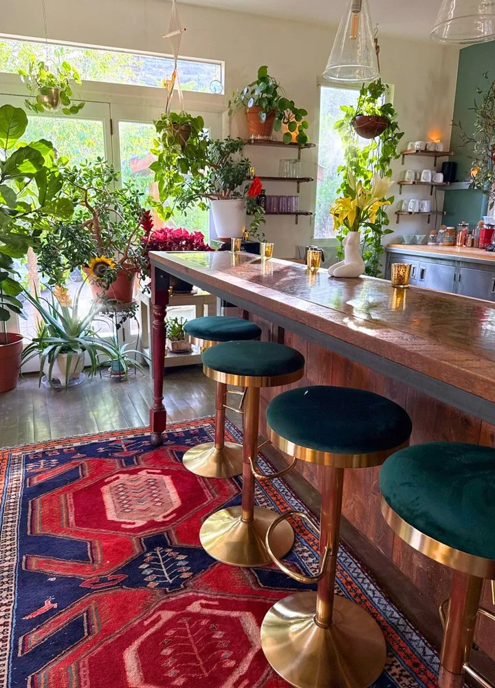 A cozy kitchen with a wooden bar counter and three modern gold and teal bar stools at Joytown, a transformational retreat & tantra sanctuary in Colorado.