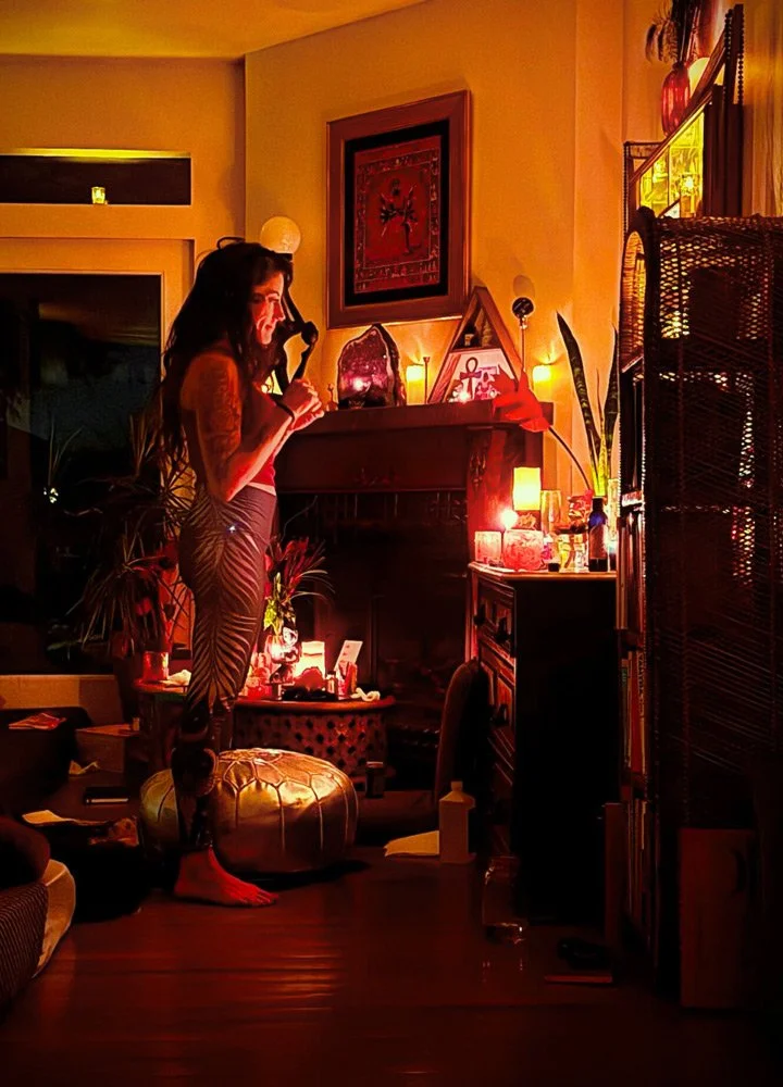 A woman standing barefoot on a large gold ottoman in a dimly lit room at Joytown, a transformational retreat & tantra sanctuary in Colorado.