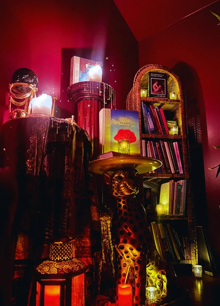 A dark red room featuring a tall bookshelf filled with books, decorative candles, and artwork at Joytown, a transformational retreat & tantra sanctuary in Colorado.