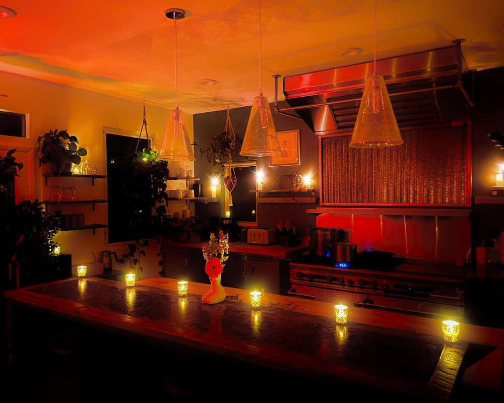 A cozy, dimly-lit kitchen with a large wooden island counter illuminated by small candles at Joytown, a transformational retreat & tantra sanctuary in Colorado.