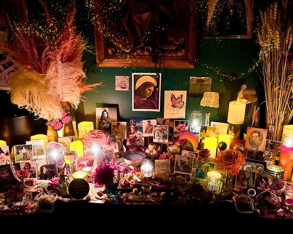 A memorial altar with photos, candles, flowers, and personal items, decorated with feathers and butterflies, set against a green wall with artwork and notes at Joytown, a transformational retreat & tantra sanctuary in Colorado.