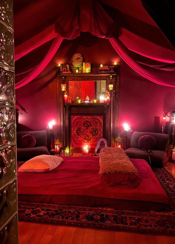 A cozy room with a red canopy, illuminated by multiple candles at Joytown, a transformational retreat & tantra sanctuary in Colorado.