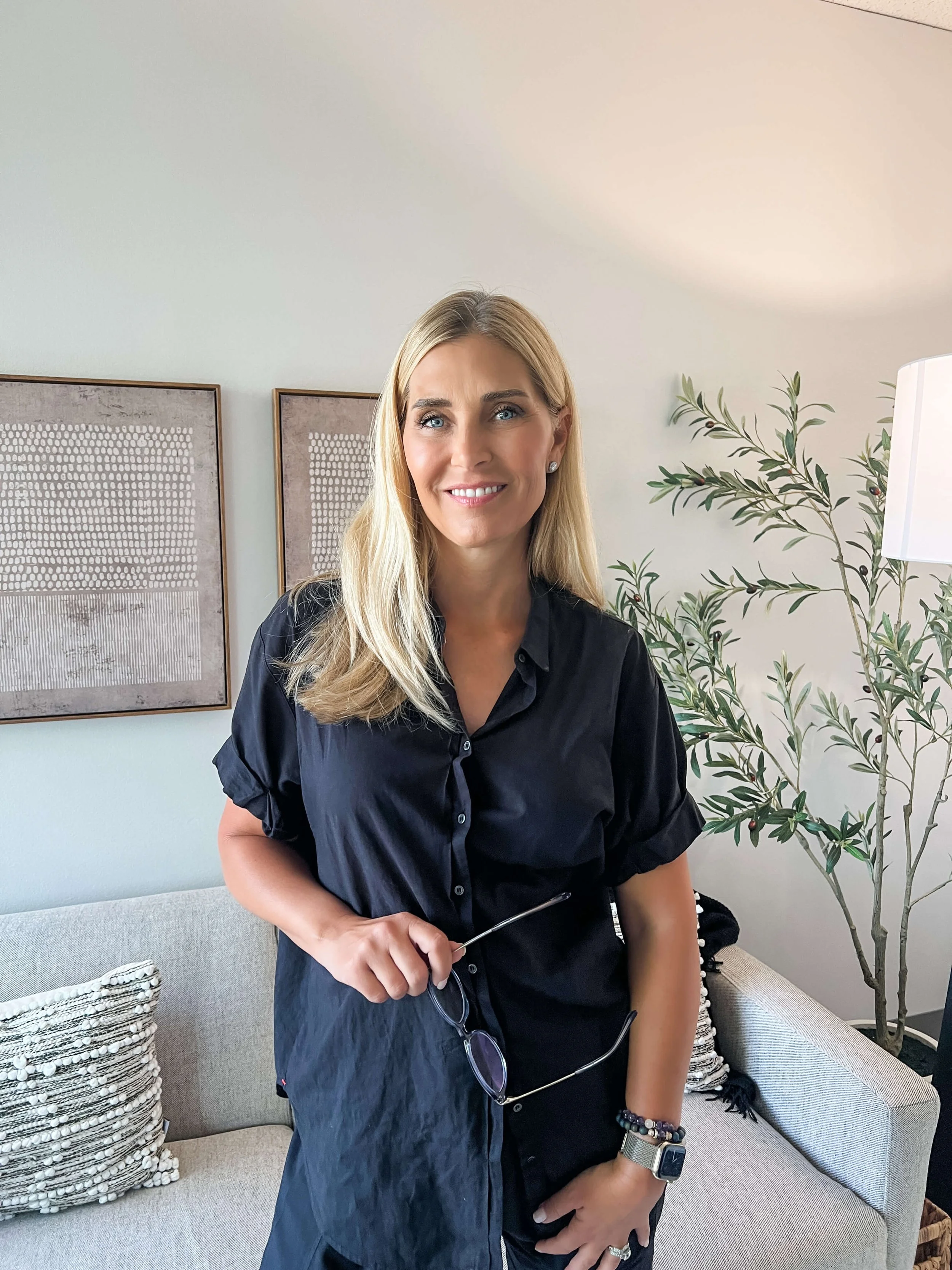 Dr. Amy. A women with blonde hair black shirt holding glasses with a calming warm smile