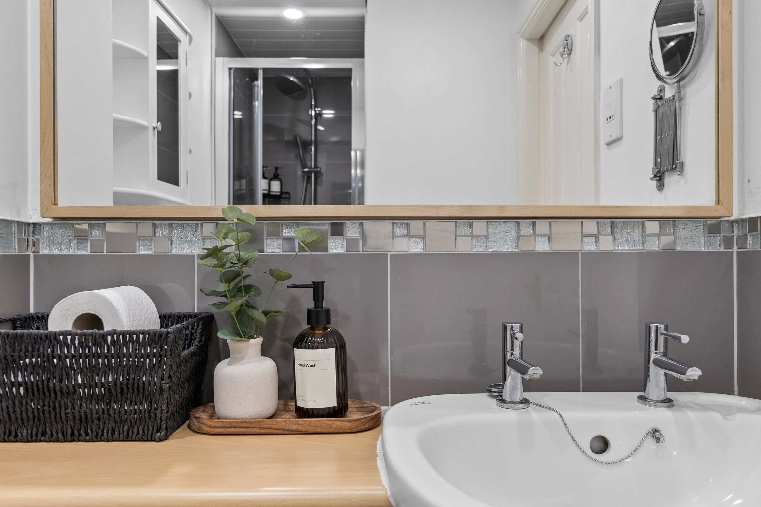 Bathroom basin with mirror and toiletries, with the shower visible in the reflection, at our Hamilton accommodation in Leicester.