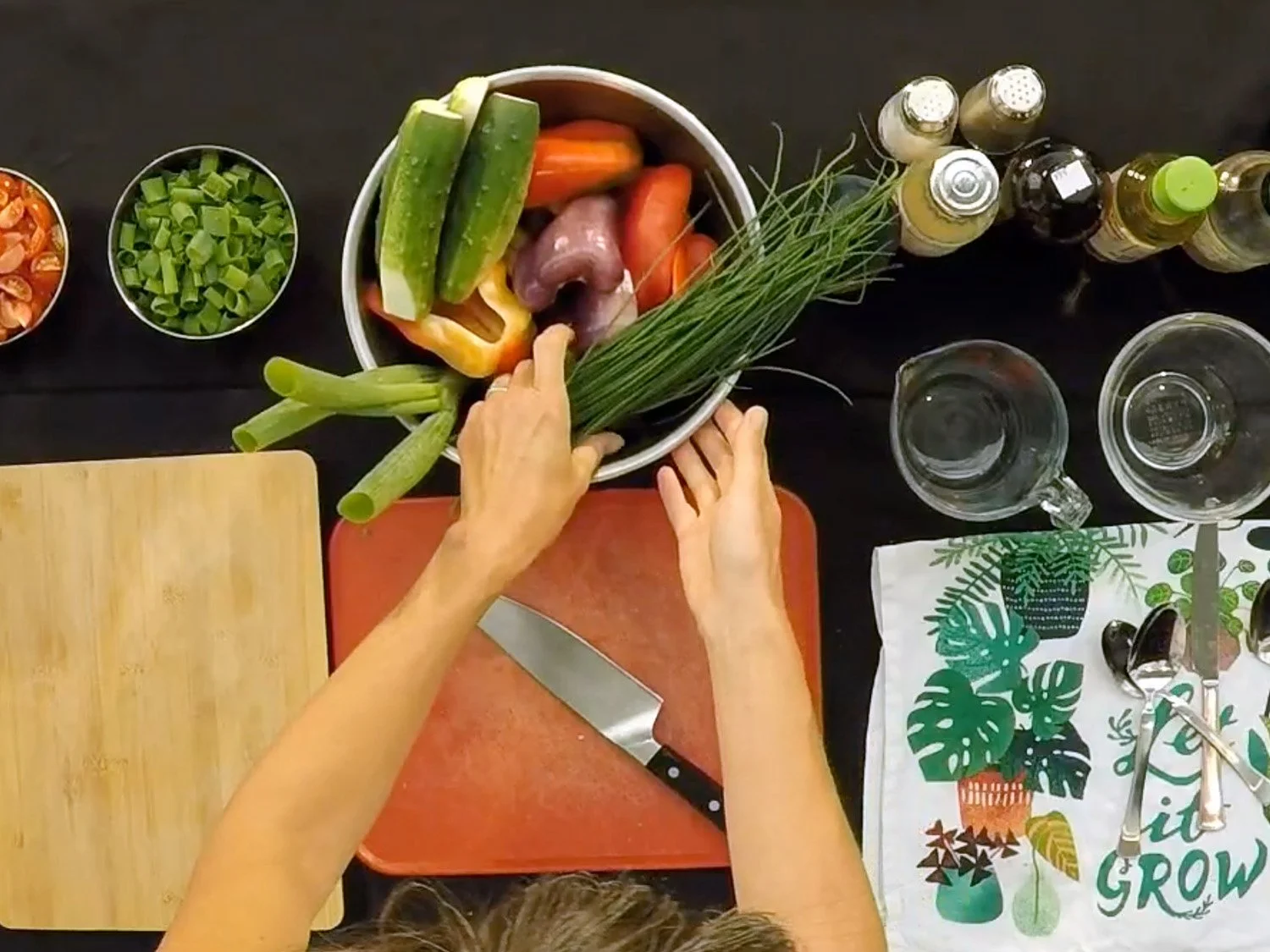A kitchen food prep area with cutting board, measuring cups, and a woman's hands reaching into a bowl of vegetables.