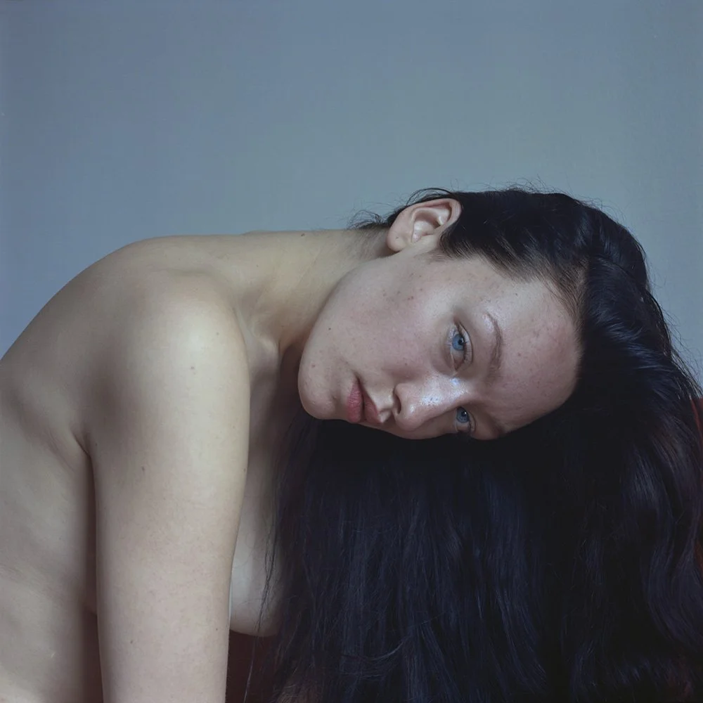 Ragazza con pelle chiara e capelli lunghi e scuri che poggia la testa su una spalla, viso leggermente rivolto verso la fotocamera