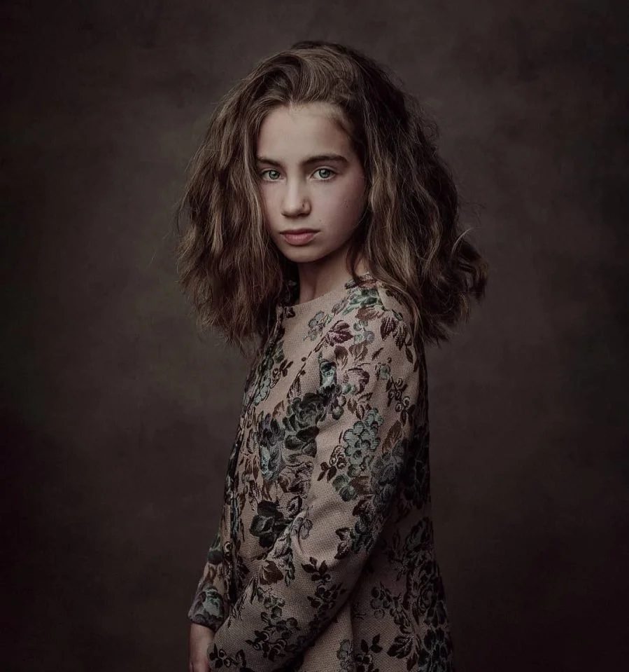 Ragazza con capelli ricci e capelli castani, indossa un vestito con motivo floreale, sfondo scuro.