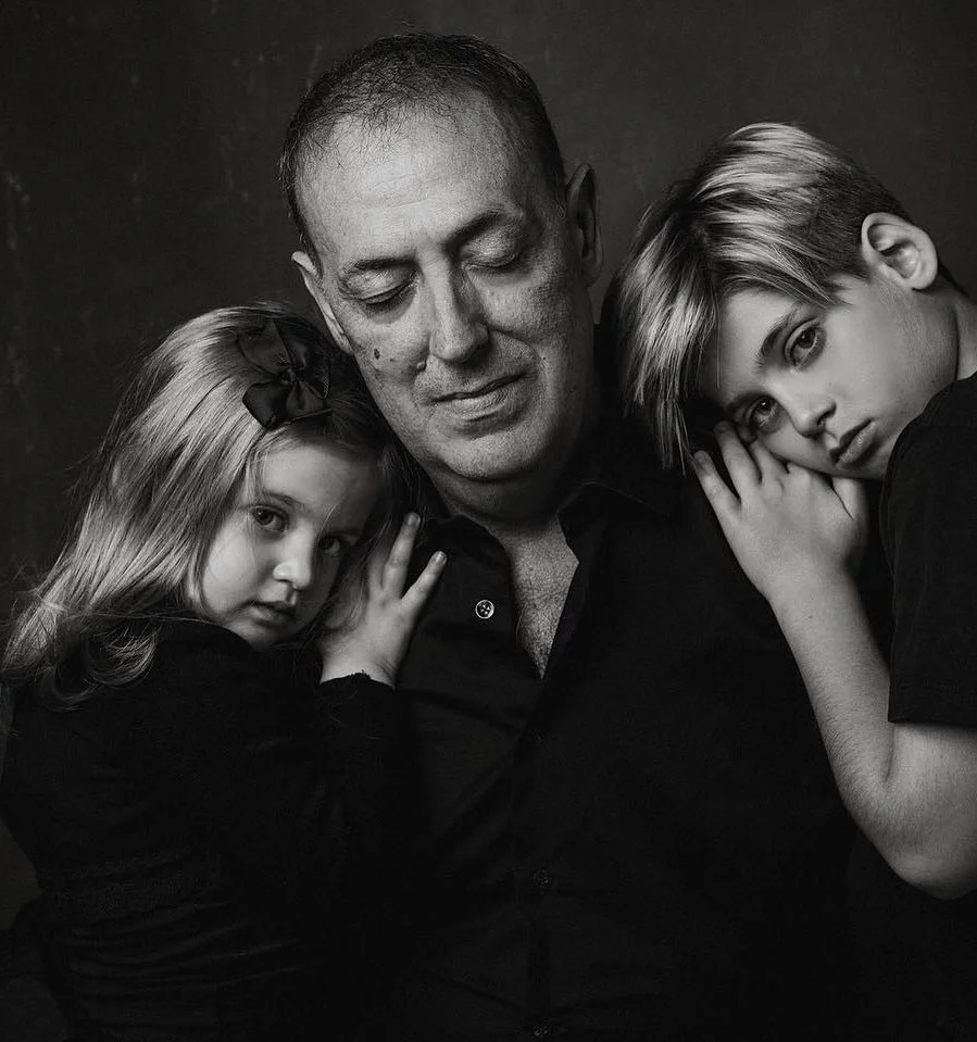 Un uomo con due bambine, una a sinistra e una a destra, in un ritratto in bianco e nero che mostra affetto e intimità.