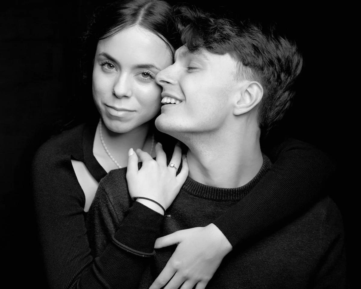 Una coppia giovane e felice abbracciata, con il ragazzo che sorride e si avvicina alla ragazza, in un'immagine in bianco e nero.