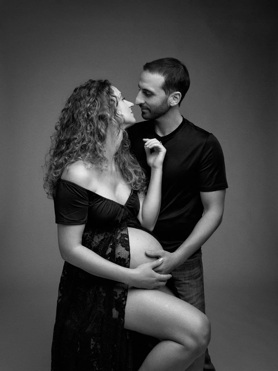 Una donna incinta e un uomo si guardano intensamente, lei si appoggia alla sua pancia e lui la tiene dolcemente, in un'immagine in bianco e nero.