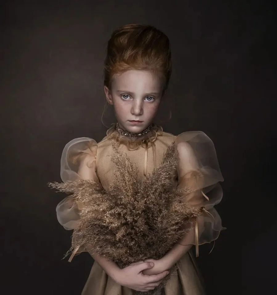 Ragazza giovane con capelli rossi, vestita con abito elegante beige e con un collo di perline, tiene un mazzo di fiori secchi.