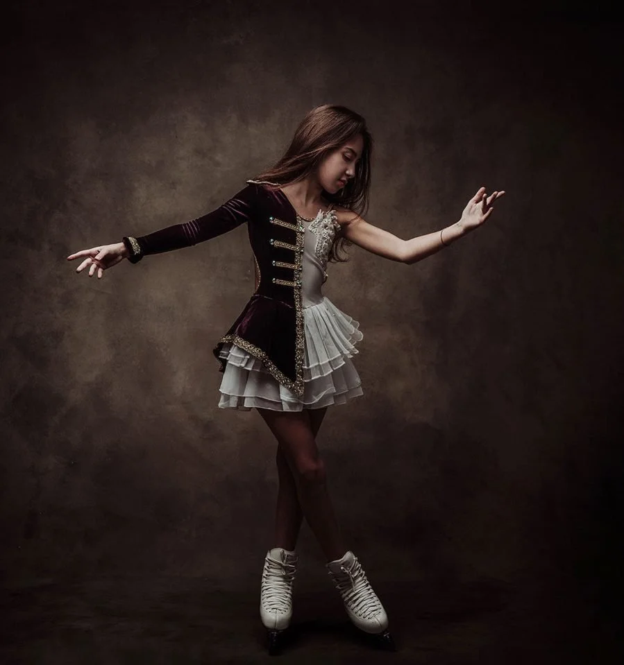 Una ragazza in abbigliamento da pattinatrice su rotelle, con un vestito decorato e scarpe da pattinaggio, posa in un ambiente con sfondo scuro.