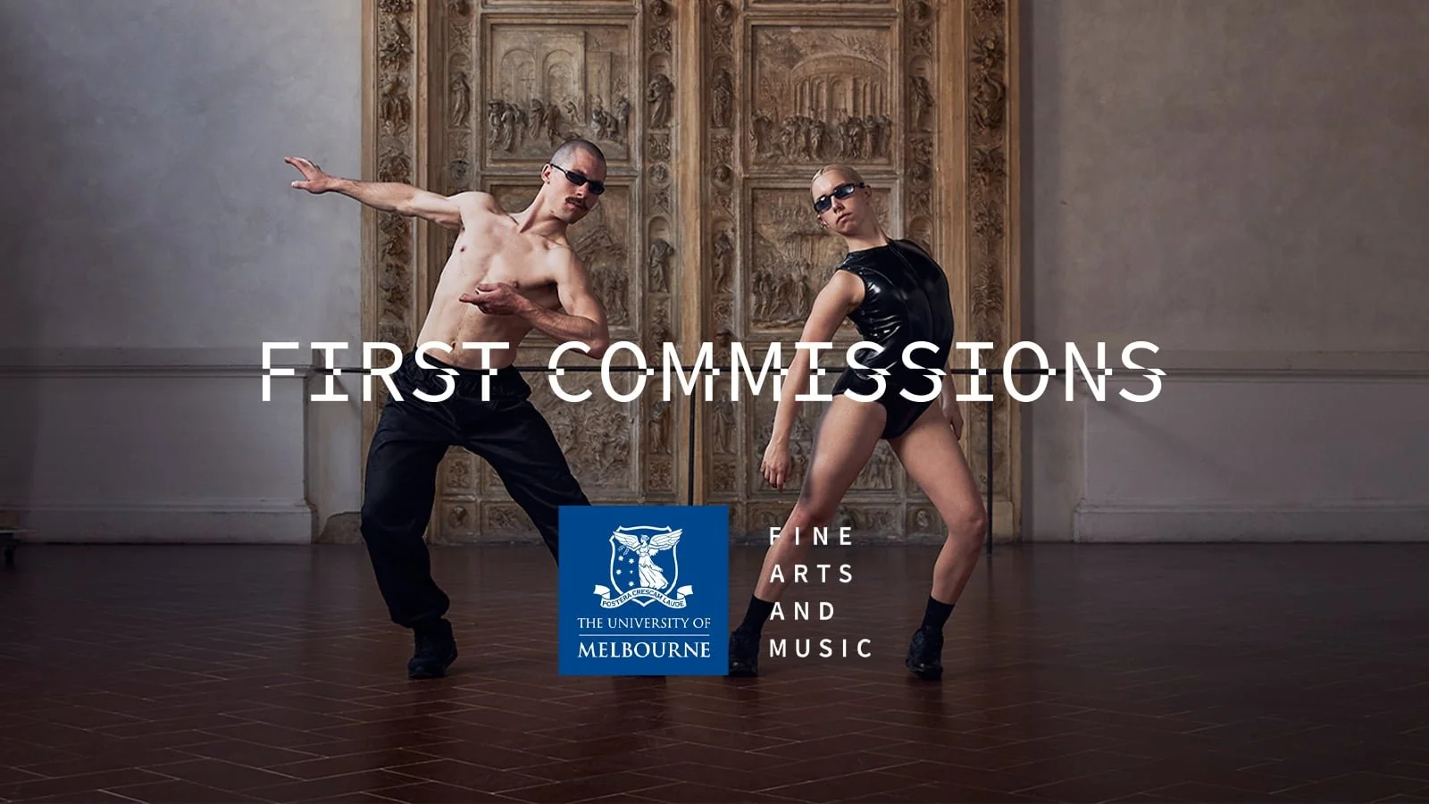 Pat Baron. Two dancers, a shirtless man with sunglasses and a woman in a black shiny dress and thigh-high boots, pose in an art gallery with ancient sculptures and a large carved wooden door in the background.