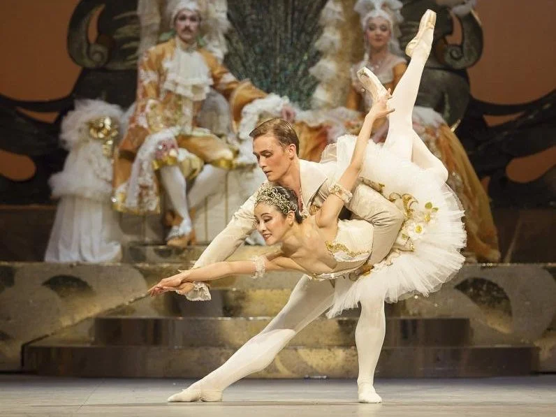 Ballet dancers performing on stage, wearing ornate costumes in a classical setting.