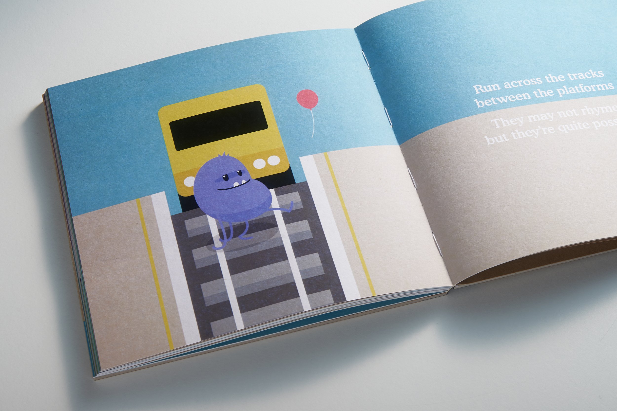 Illustrated book page with a purple character crossing train tracks in front of a yellow train, with a red balloon and text on the opposite page.