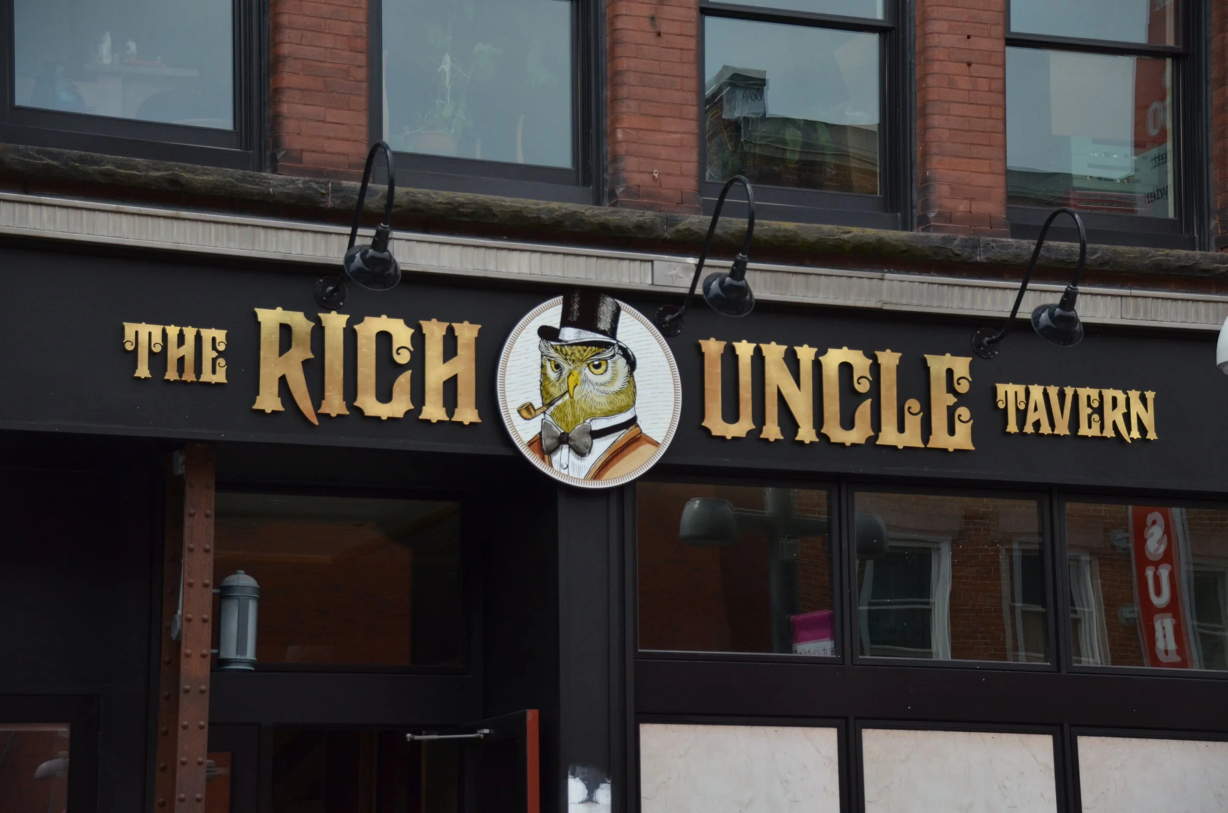 Downtown Kitchener Rich Uncle Fascia signage Router cut dimensional acrylic lettering with 23kt gold leaf and circular logo