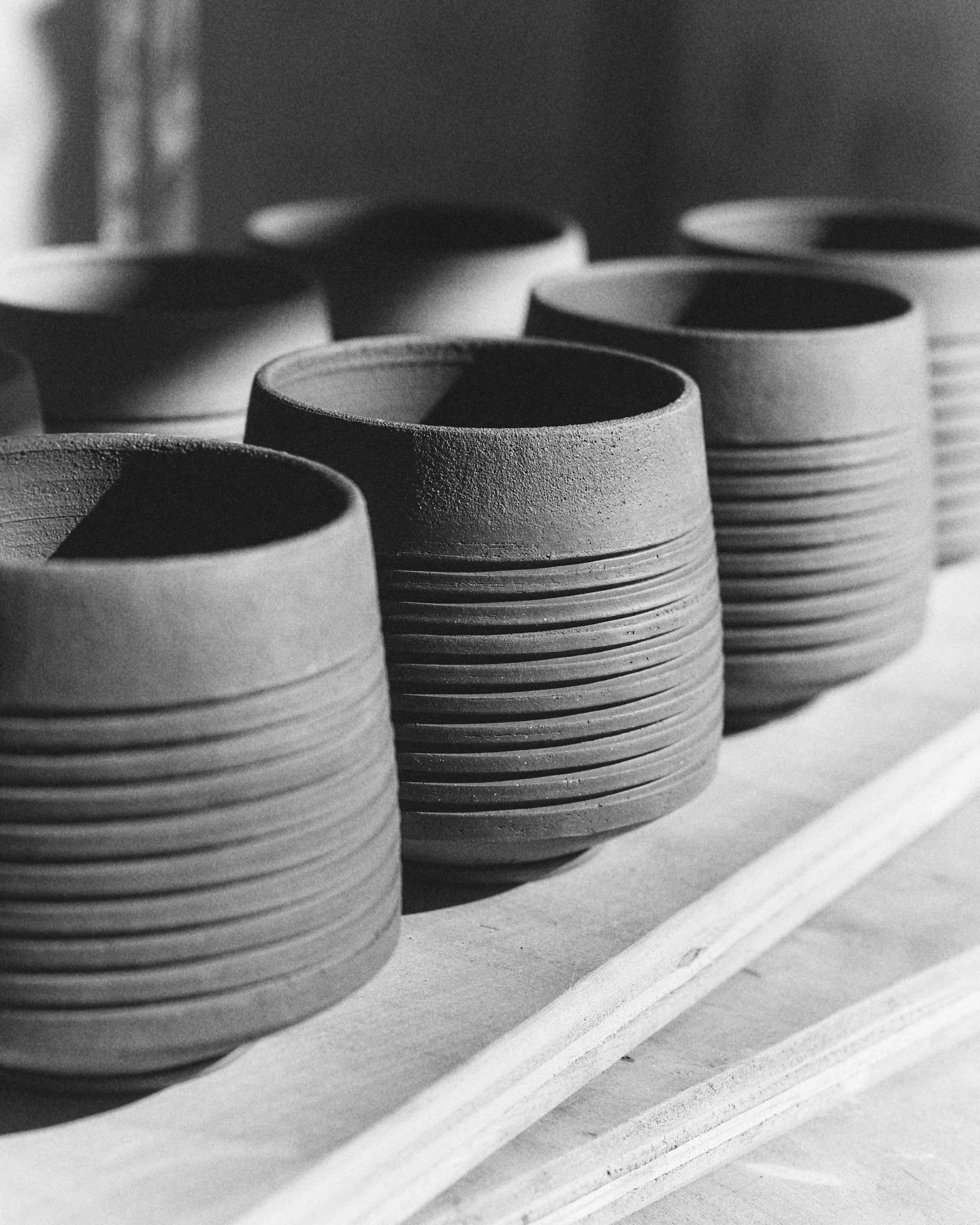 Black and white image of multiple ceramic cups with ridged designs placed on a wooden surface Dan Mack Studio.