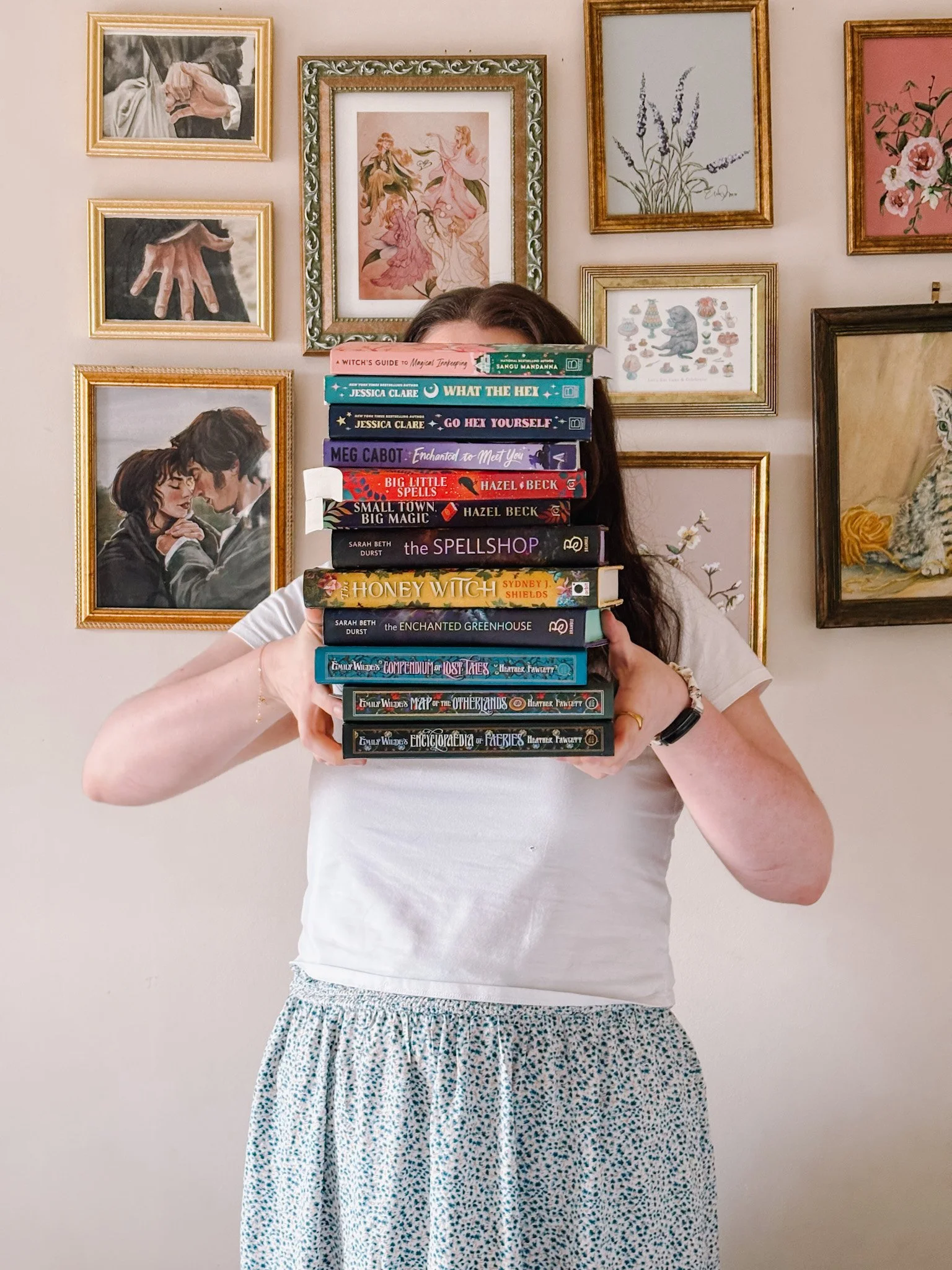 Next Era Influence founder and marketing strategist Sarah Walsh holding a stack of romance and fantasy books in front of a gallery wall.
