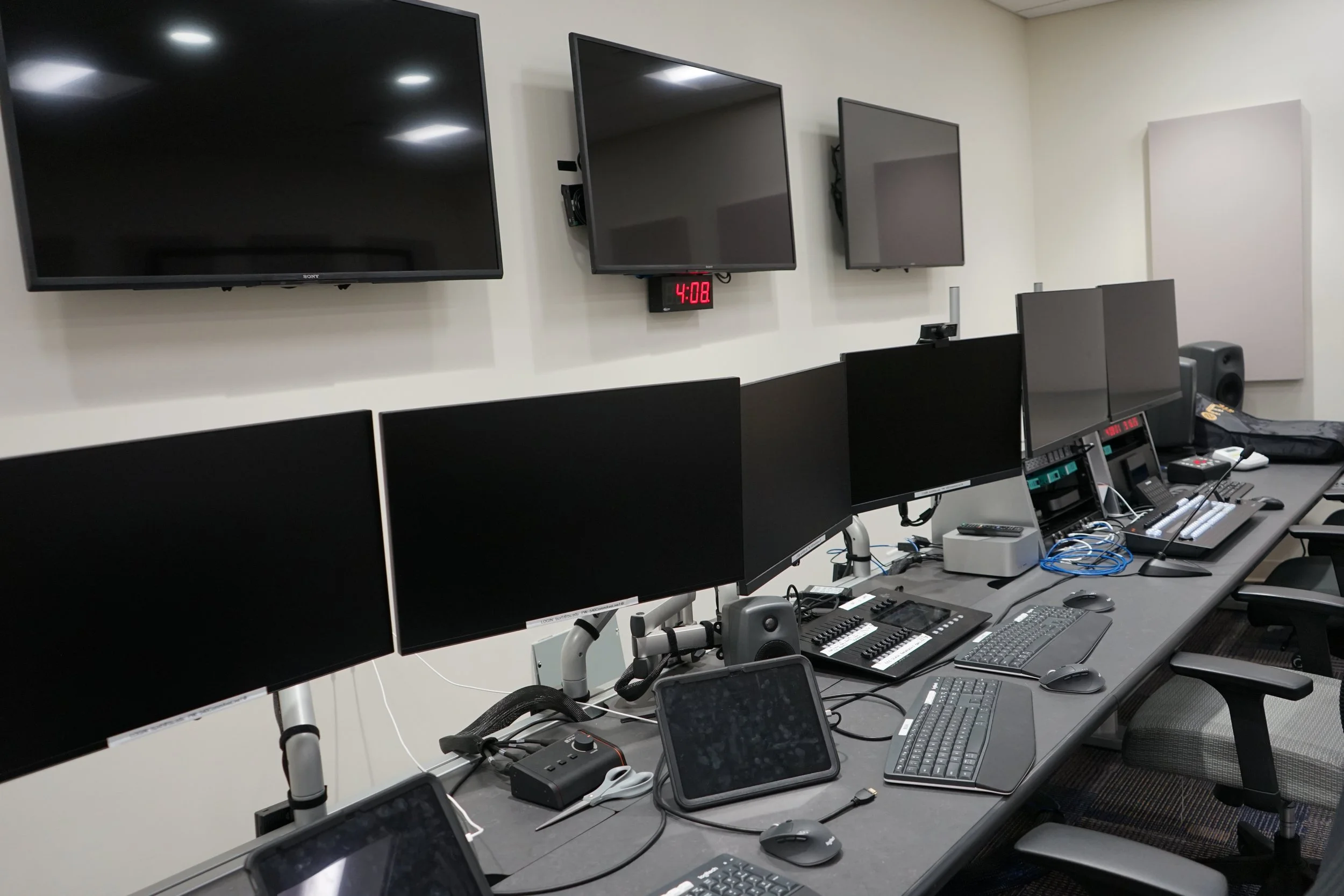 Modern video and audio production control room with multiple monitors, mixer, keyboards, speakers, and broadcast equipment.