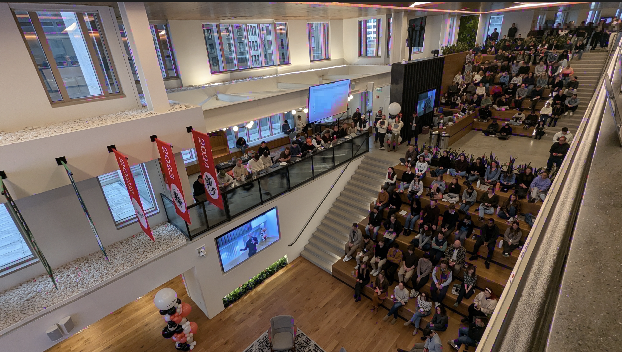 Interior view of a crowded multi-level auditorium, large screens displaying presentations.