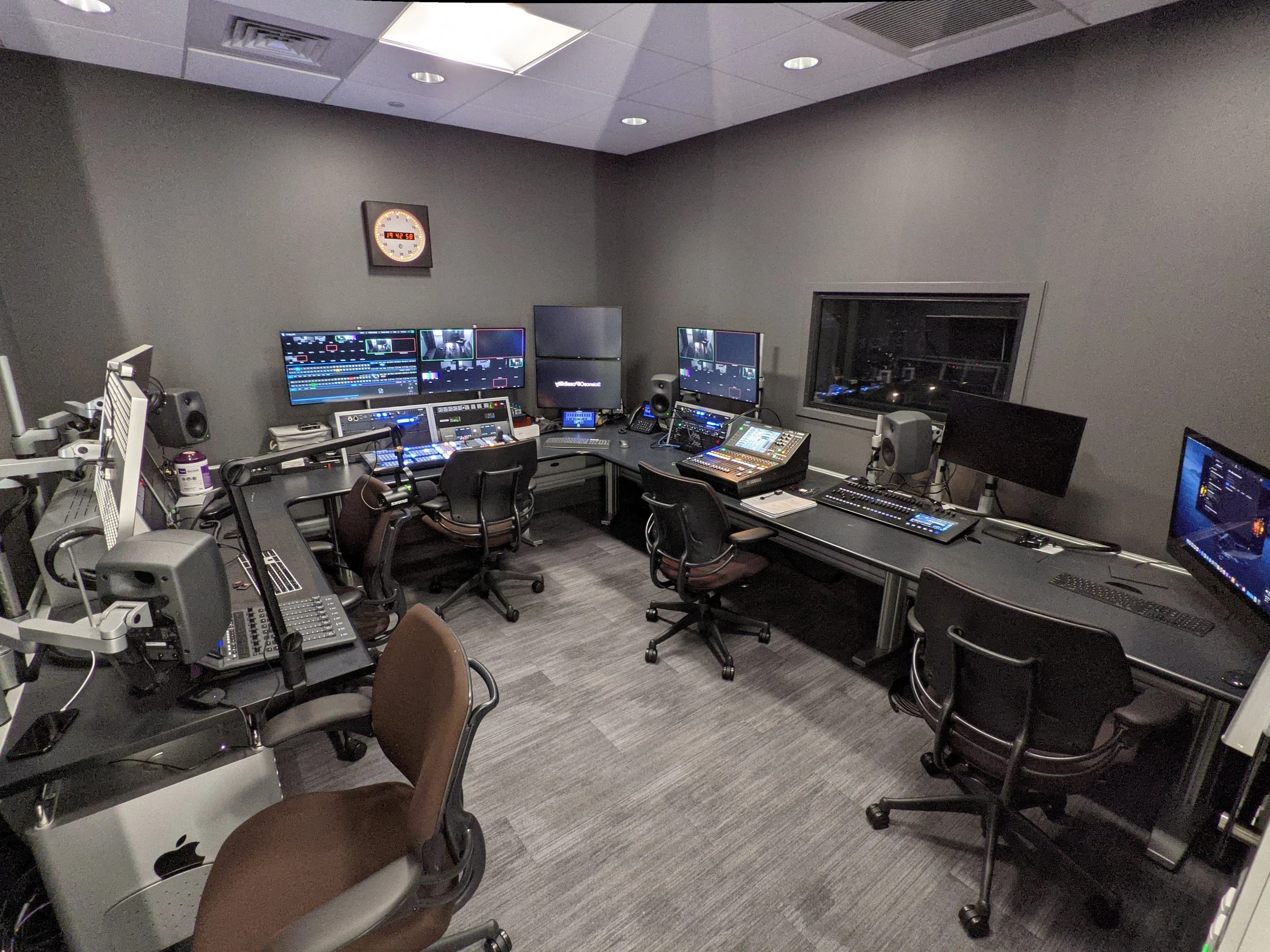 Video and audio control room with multiple monitors, computers, and mixing equipment.