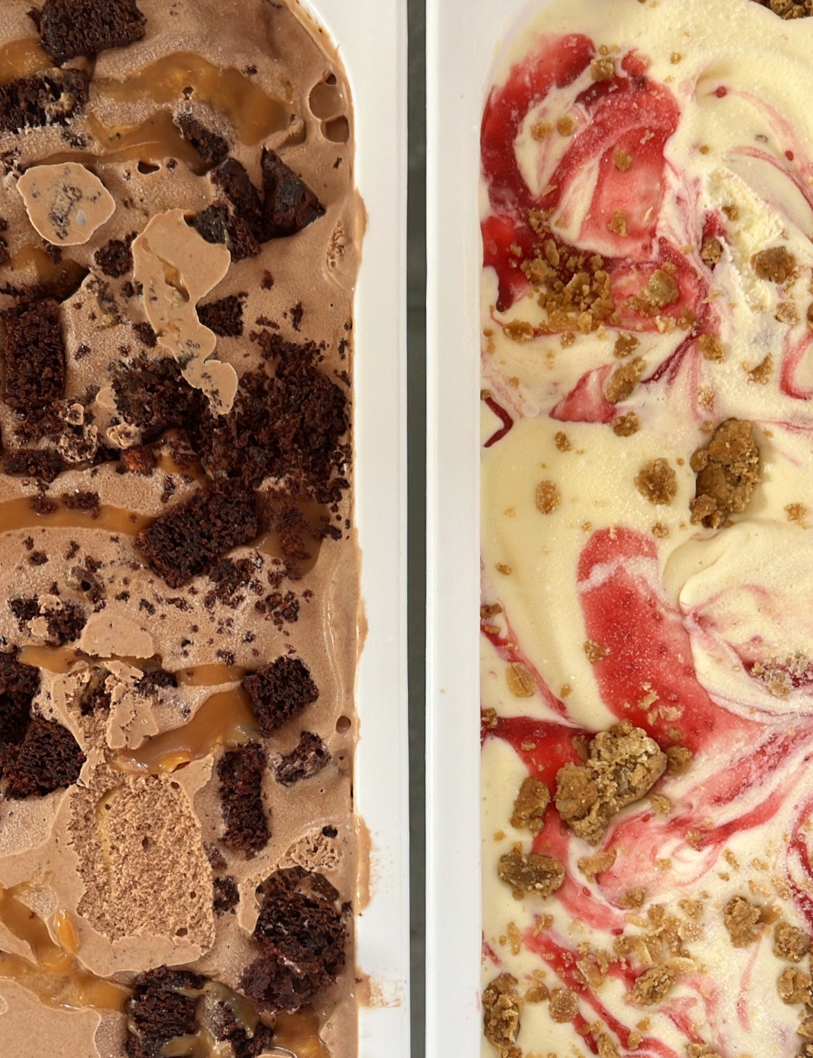 Two ice cream flavors in white rectangular containers. The left flavor is chocolate with chocolate chunks and caramel swirls. The right flavor is vanilla with raspberry sauce and cookie crumbles.