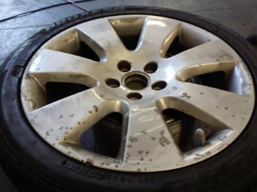 A used car wheel with a dirty, scratched beige alloy rim and tire mounted on it.