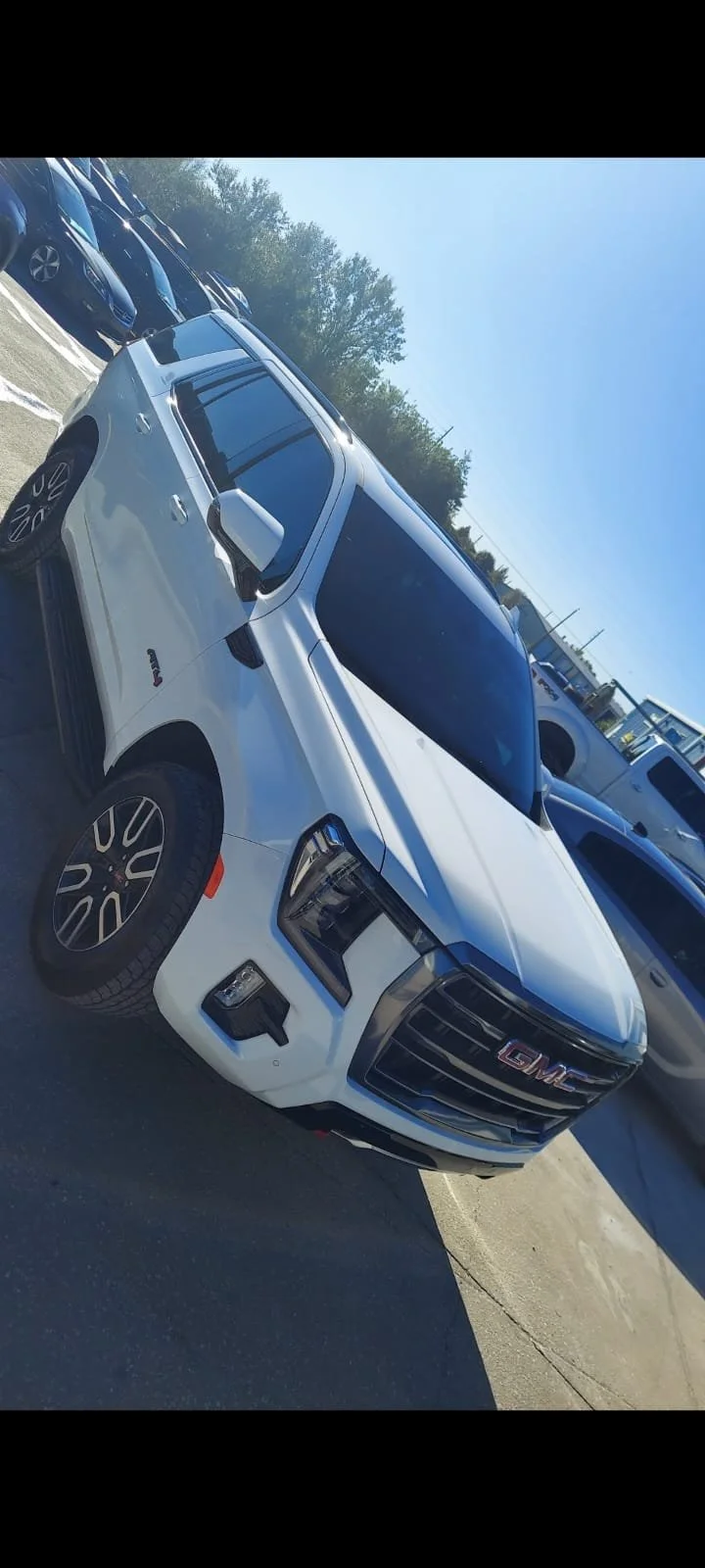 White GMC pickup truck parked in a parking lot with other vehicles and trees in the background on a sunny day.