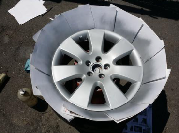 Car wheel surrounded by a protective cardboard ring, placed on pavement outdoors.