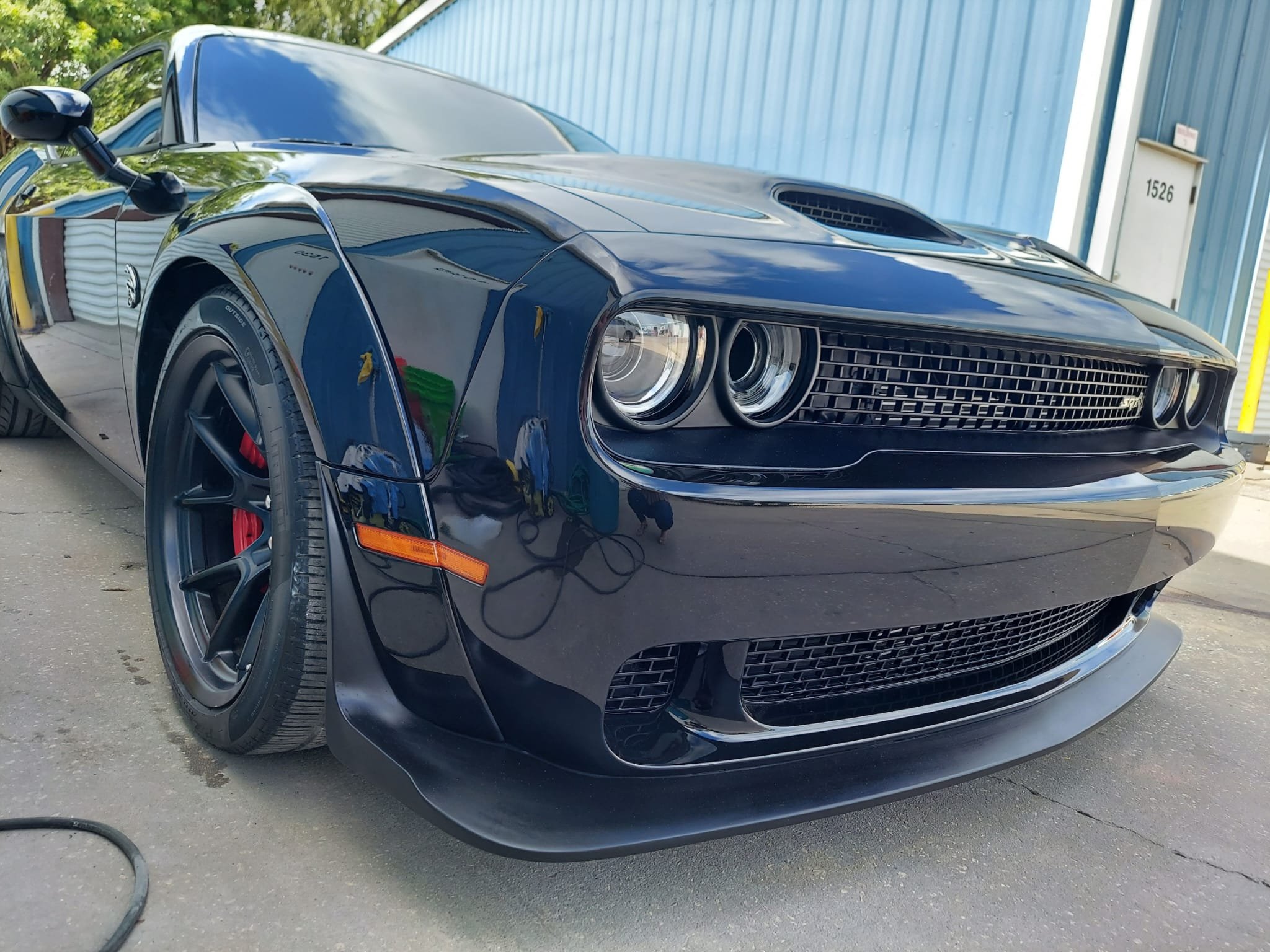Black Dodge Challenger with a glossy finish parked outdoors near a blue building.