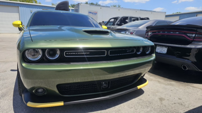 Front view of a green Dodge Challenger with black accents parked in a lot, surrounded by other cars.