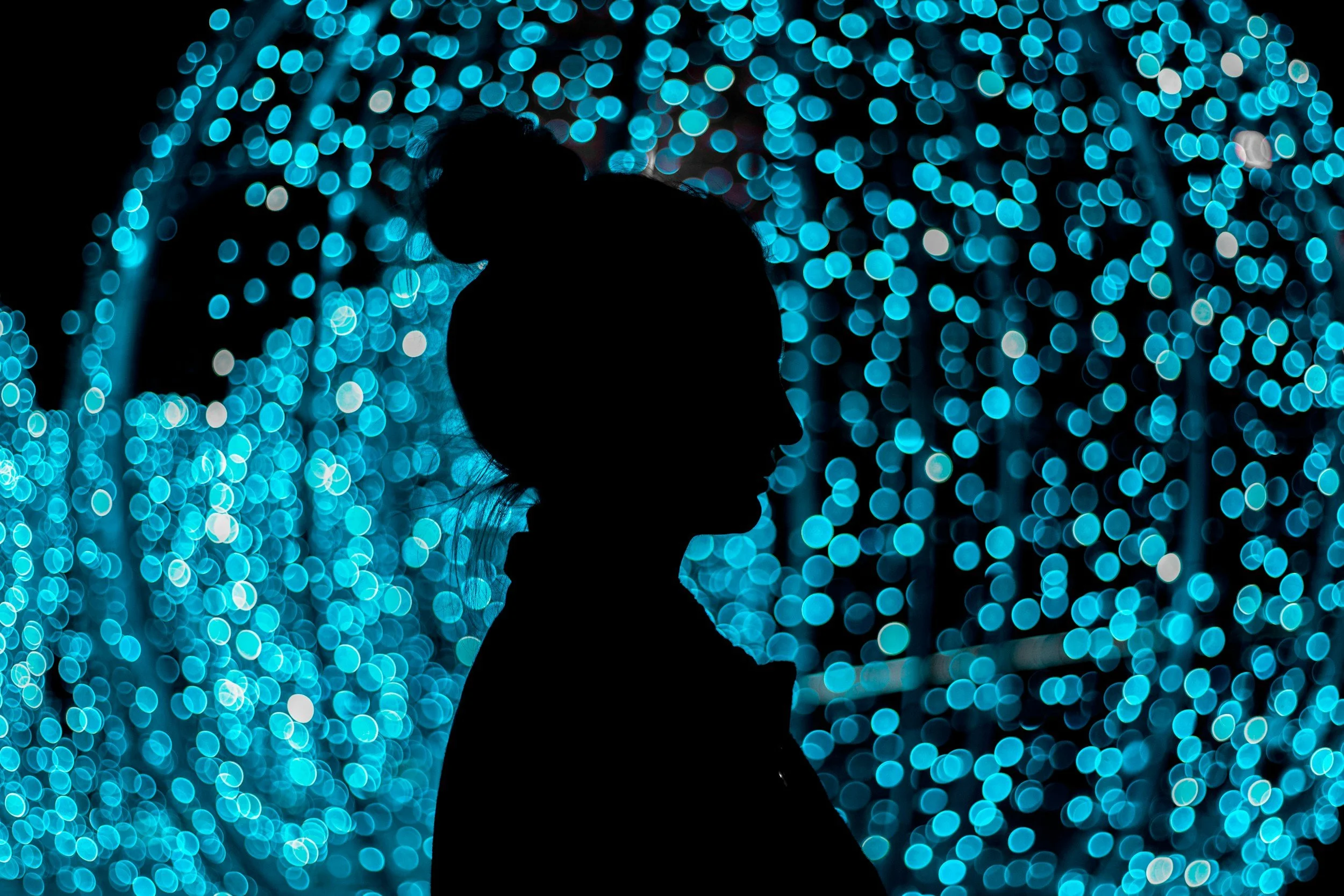 Silhouette of a woman with a top bun hairstyle standing against a background of blue and white bokeh lights.