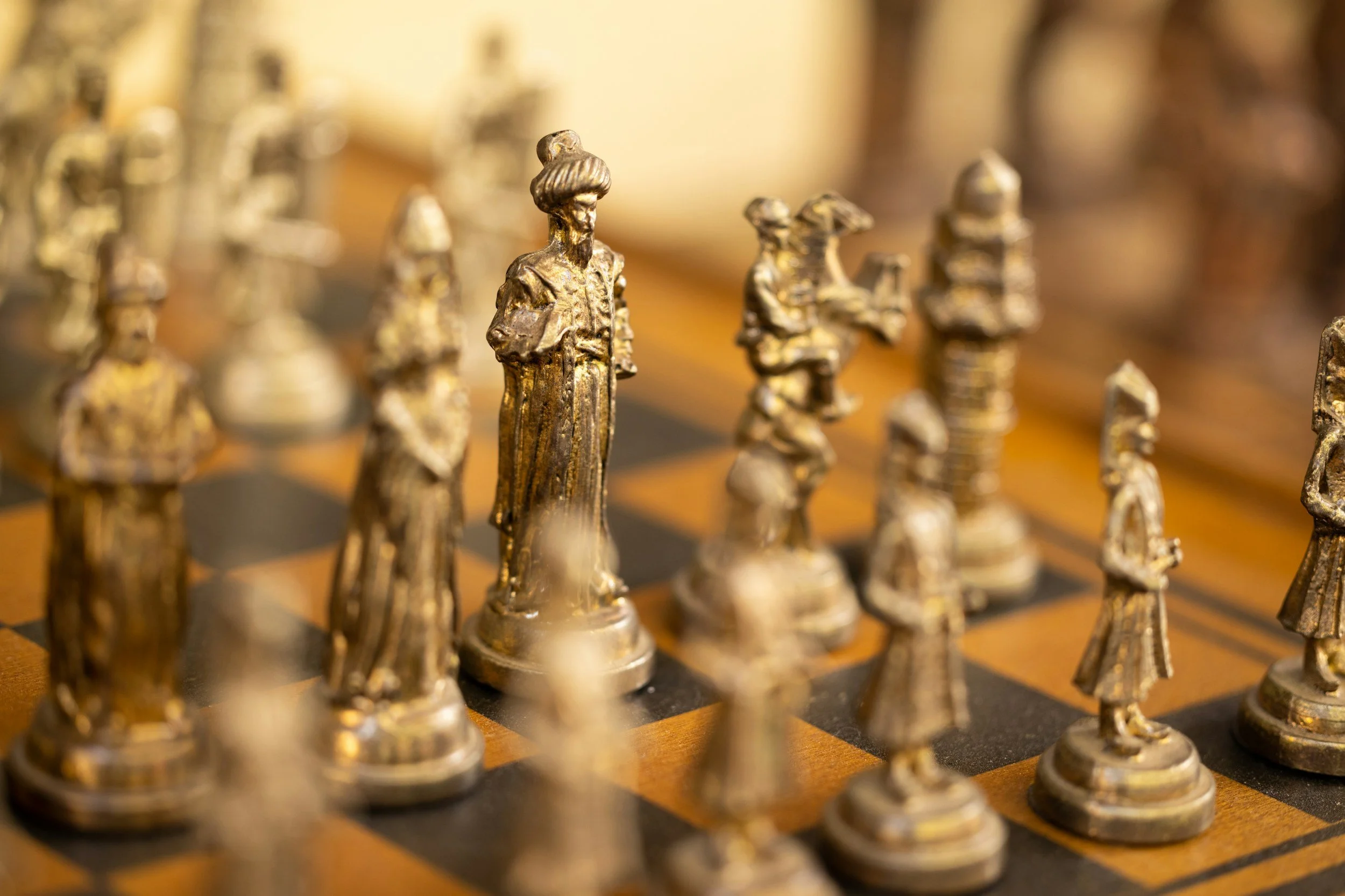 Close-up of brass chess pieces on a chessboard, focusing on the king and surrounding pieces.