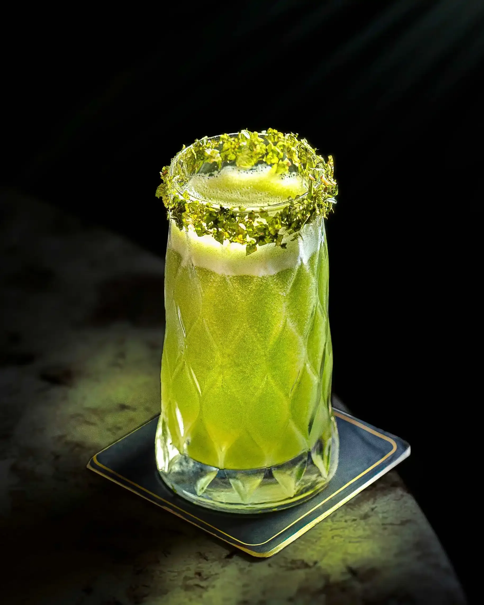 Professional beverage photography of a green cocktail with a garnished rim, utilizing dramatic lighting and texture to elevate the drink's presentation.