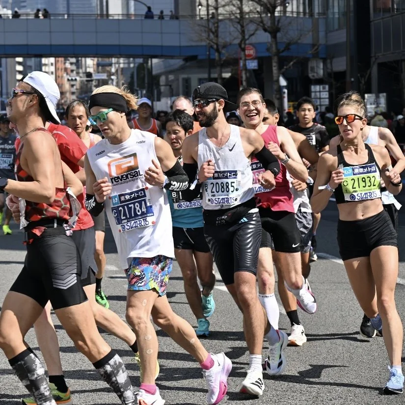 Group of runners participating in a marathon, showing legs and shoes on a street surface.