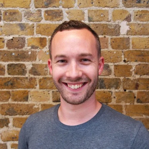 Person smiling in front of a brick wall.