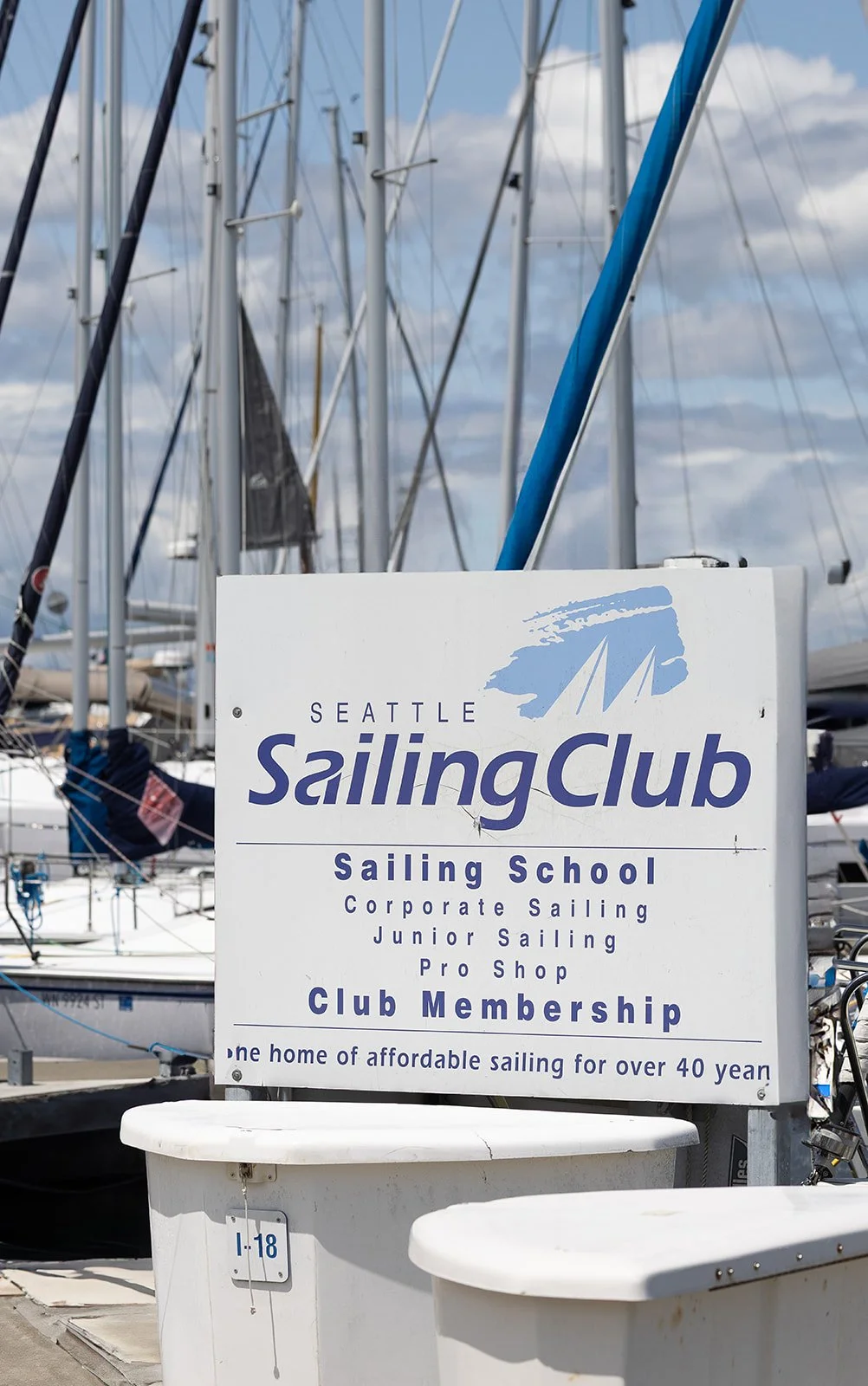Sign for Seattle Sailing Club at a marina with sailboats in background.