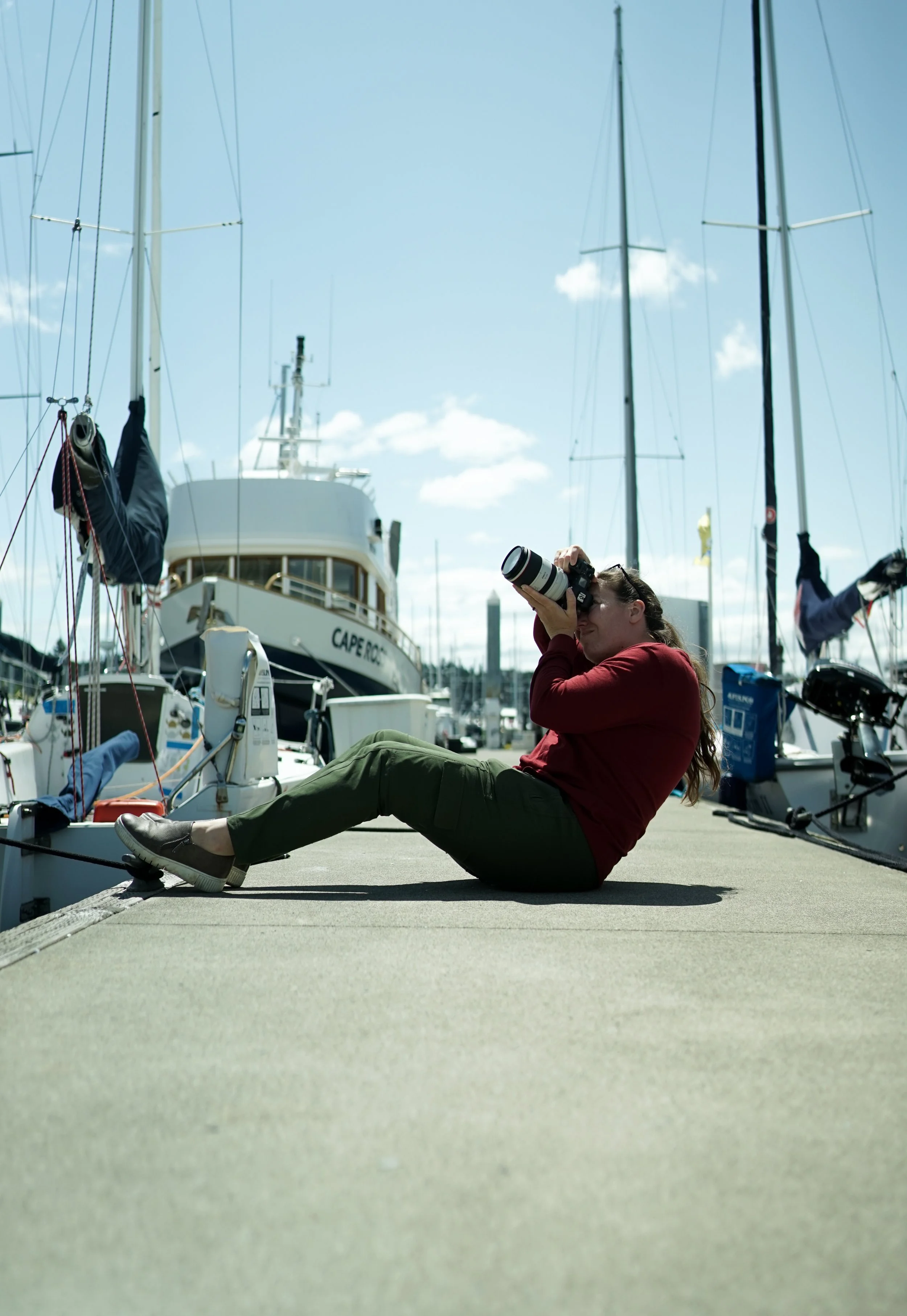woman sitting on a dock in a marina taking a photo with a dslr camera and lens