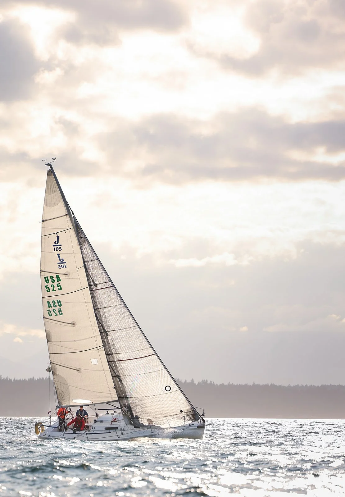 A sailboat with two sails on a body of water under a cloudy sky.
