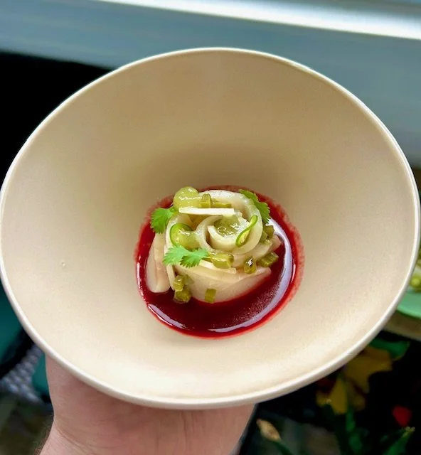 A small dish with sliced vegetables, cilantro, and green onions in a red sauce in a white bowl.