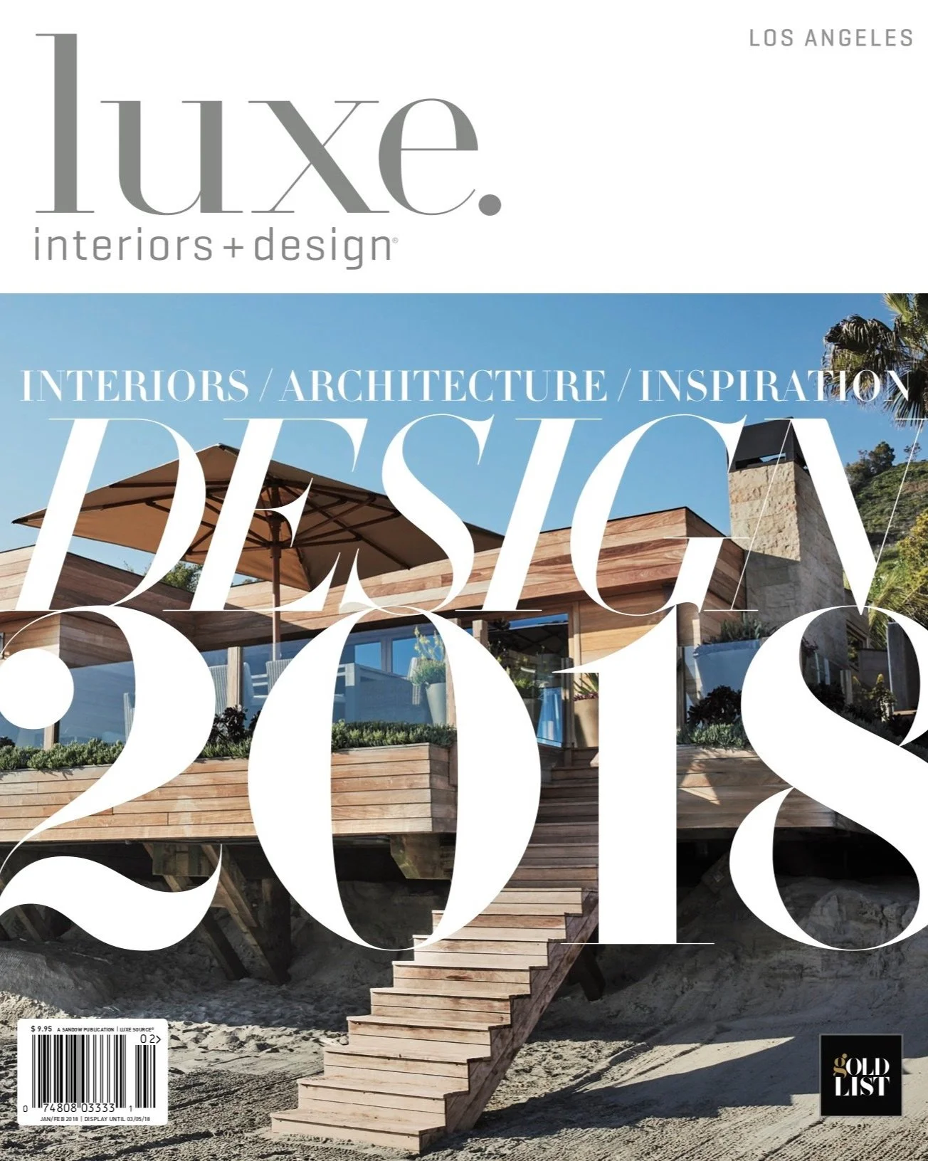 Front cover of Luxe Interiors + Design magazine, January/February 2018 issue, featuring a modern wooden house with an outdoor deck and sun umbrella, set on a sandy beach under a clear blue sky.
