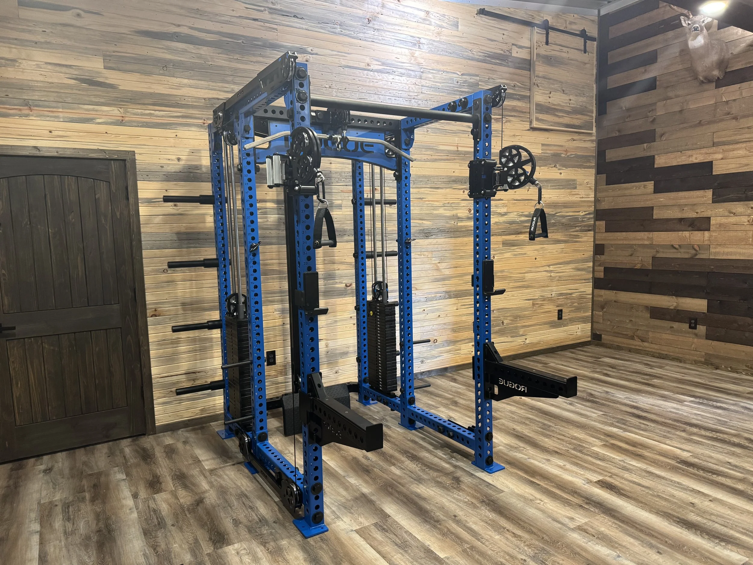 Blue multifunctional squat rack with pull-up bars and weight storage in a home gym with wooden walls and floor.