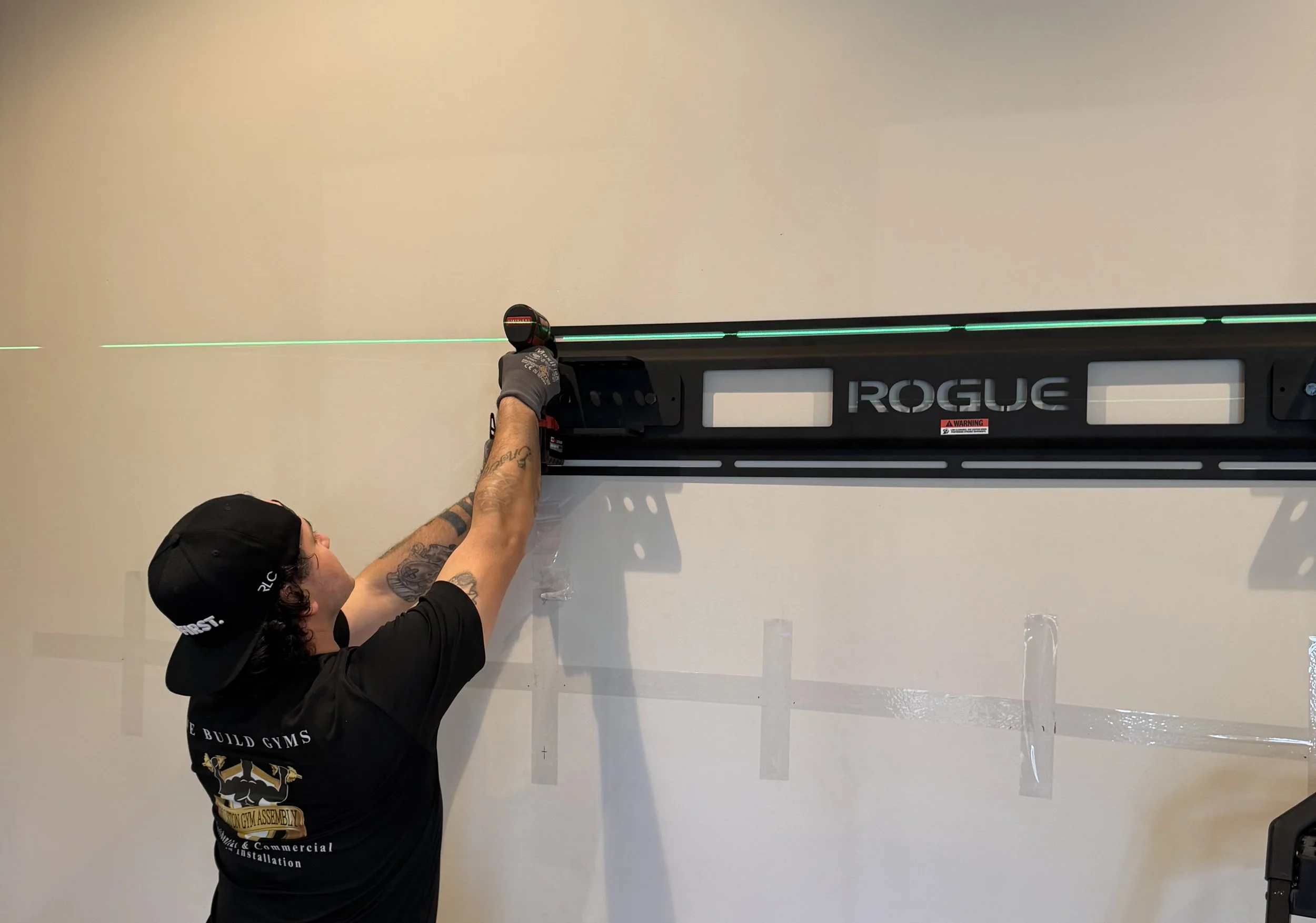 Houston Gym Assembly technician precision leveling a Rogue Fitness wall-mounted rack.