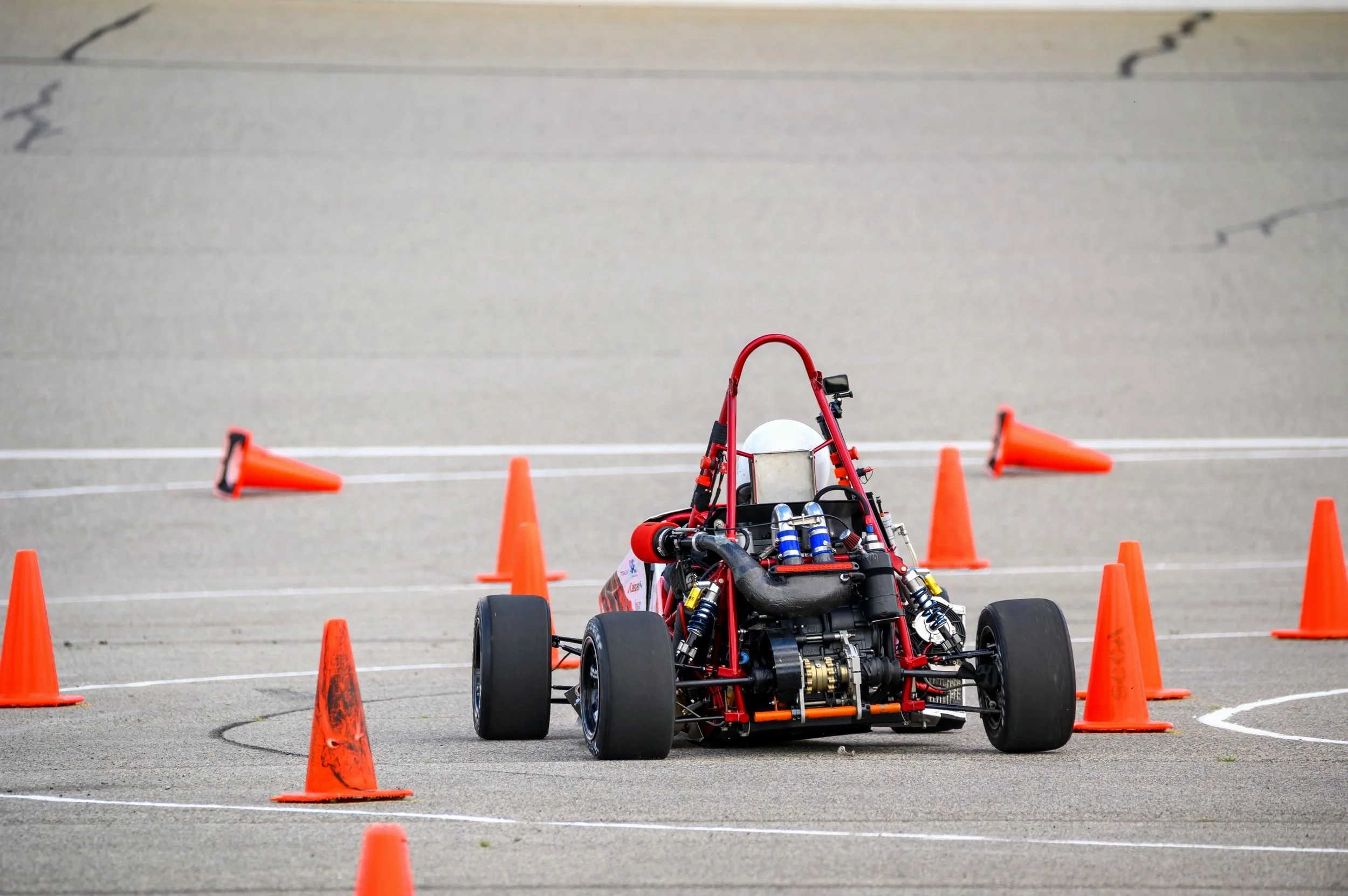 A race car navigating through orange cones on an asphalt track.