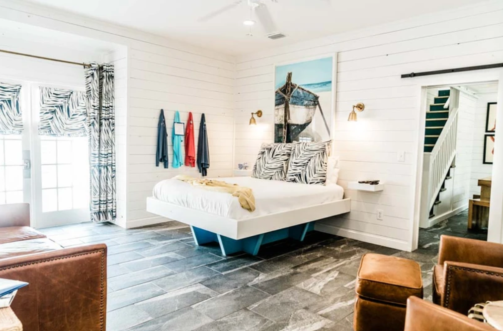 Bedroom with a modern floating bed, white shiplap walls, and nautical decor. Features patterned curtains, a small staircase, and seating area with leather furniture.