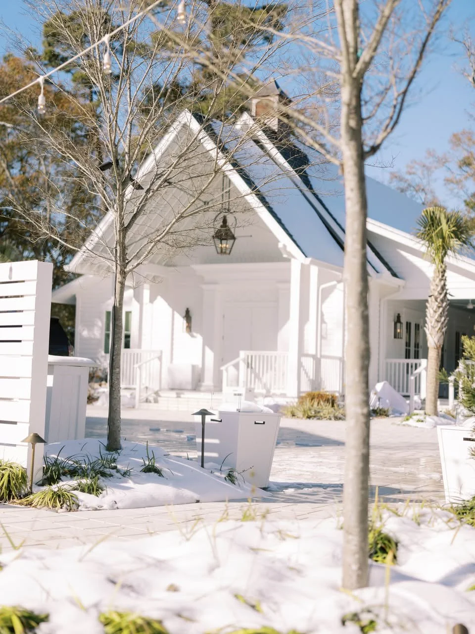 White house with snowy landscape, bare trees, and a clear blue sky.