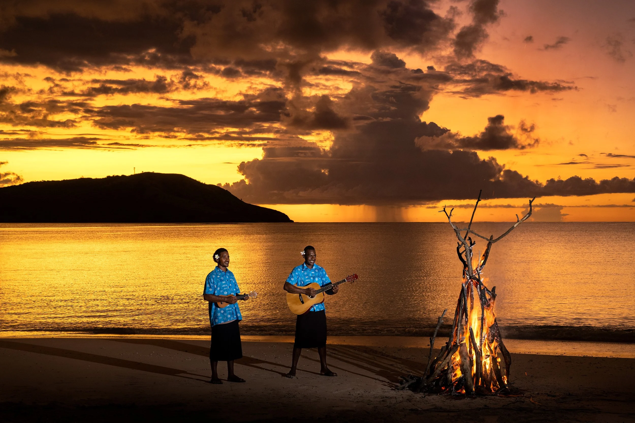 Fijian musicians beside a beach bonfire at sunset in the Yasawa Islands