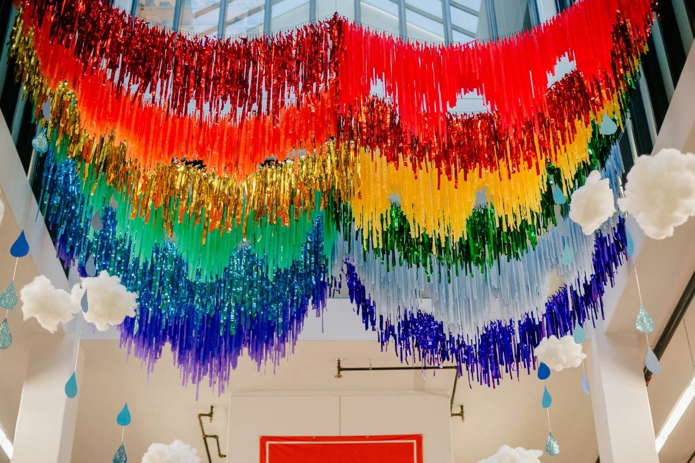 Colorful aerial fringe decorations in rainbow order with cotton clouds and raindrop shapes in hanging from the venue ceiling.