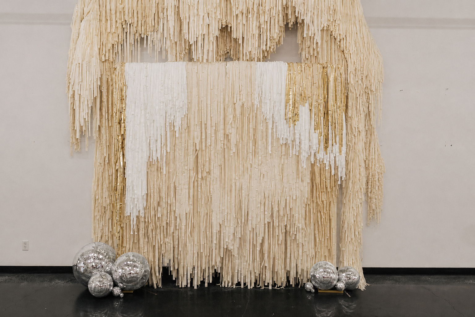 Decorative Fringe backdrop with cream and white strips hanging vertically, accented with gold strips, and several disco ball ornaments on the floor.